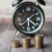 Stacked coins and a classic alarm clock symbolize the value of time and money.