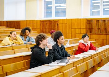 Students of various backgrounds attentively listening in a university lecture hall.