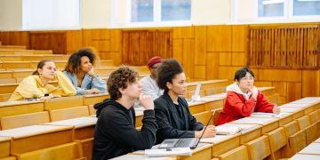 Students of various backgrounds attentively listening in a university lecture hall.