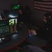 Cybersecurity professionals working on computer systems, focusing on data protection in a dimly lit room.