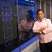 Black woman engineer with crossed arms standing in a server room, smiling confidently.