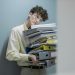 Young man overwhelmed with a stack of folders symbolizes workplace stress.
