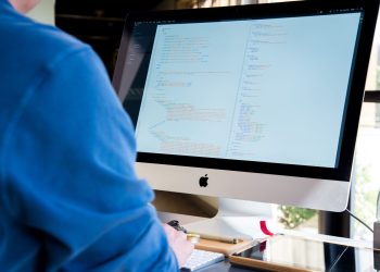 A programmer in a blue shirt coding on an iMac. Perfect for technology or work-related themes.