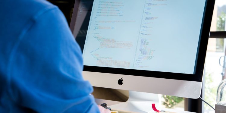 A programmer in a blue shirt coding on an iMac. Perfect for technology or work-related themes.