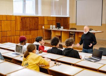 Students engaging with a professor in a university lecture hall, utilizing technology.