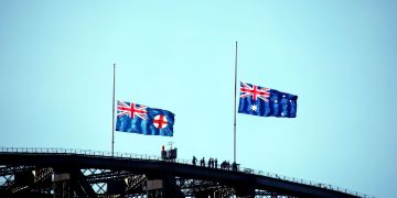 Australian and New South Wales flags flying on Sydney Harbour Bridge silhouette.