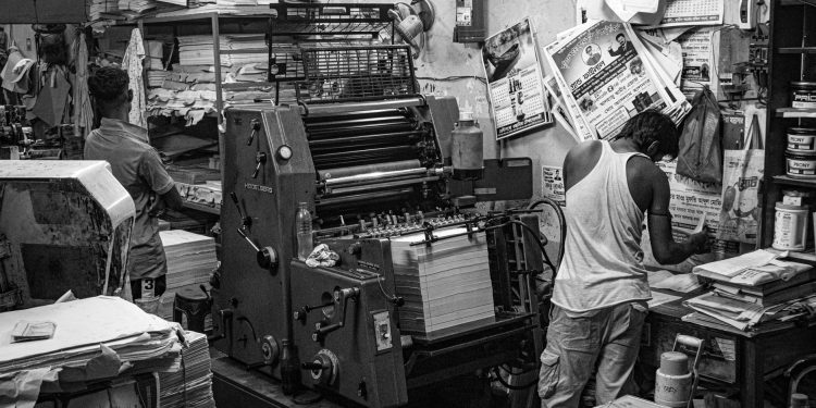 Black and white image of a bustling print shop with workers operating a printing press.