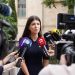 A spokesperson engages with media during an outdoor press interview surrounded by microphones.