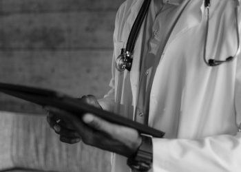 Black-and-white photo of a medical professional holding a tablet, focusing on digital health technology.