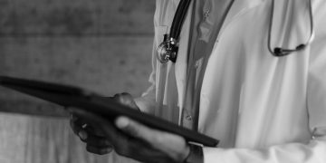 Black-and-white photo of a medical professional holding a tablet, focusing on digital health technology.