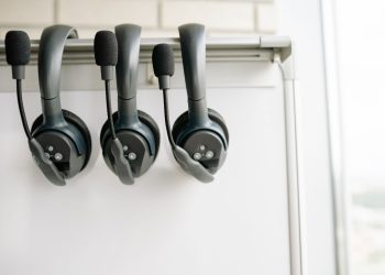 Three black headsets neatly organized on a whiteboard hook, emphasizing tech and communication.