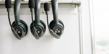 Three black headsets neatly organized on a whiteboard hook, emphasizing tech and communication.