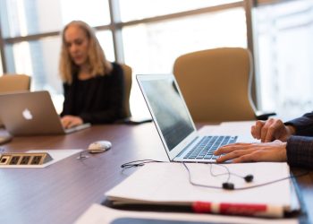 Colleagues collaborating in a bright, modern office setting, focused on laptop work.