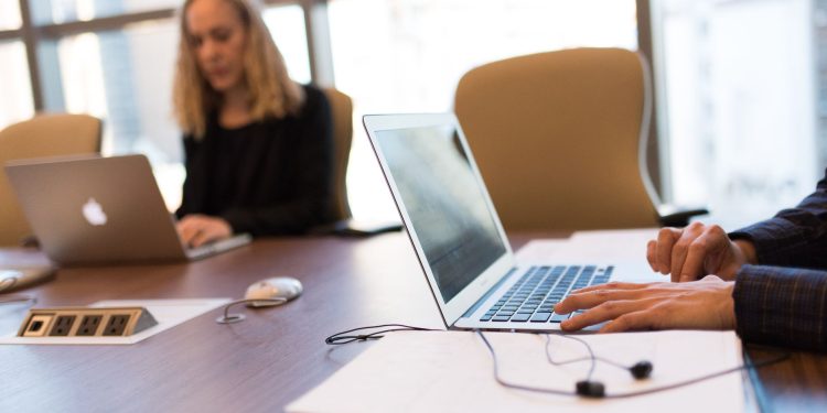 Colleagues collaborating in a bright, modern office setting, focused on laptop work.