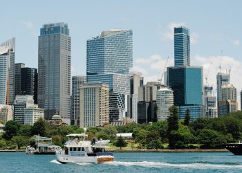 Modern Sydney skyline with vibrant blue skies, skyscrapers, and boats on the harbor.