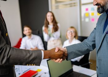 Close-up of a handshake between colleagues in a professional office setting, emphasizing teamwork and agreement.
