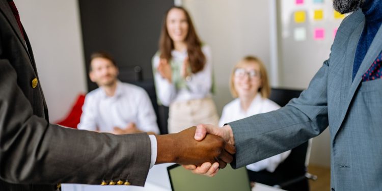 Close-up of a handshake between colleagues in a professional office setting, emphasizing teamwork and agreement.