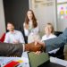 Close-up of a handshake between colleagues in a professional office setting, emphasizing teamwork and agreement.