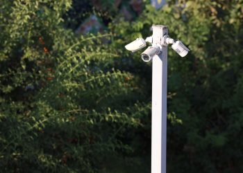 Cluster of surveillance cameras mounted outdoors amidst green foliage for public safety.