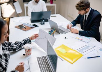 Professionals collaborating in a modern office with laptops and documents, focusing on teamwork.