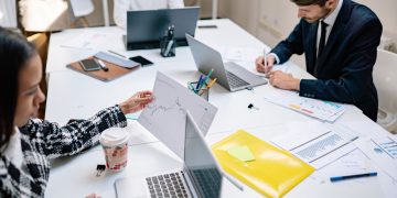 Professionals collaborating in a modern office with laptops and documents, focusing on teamwork.