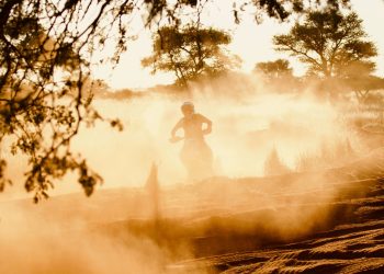 Dynamic shot of a dirt biker riding through a dusty trail with sun setting in the background.