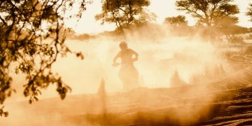 Dynamic shot of a dirt biker riding through a dusty trail with sun setting in the background.