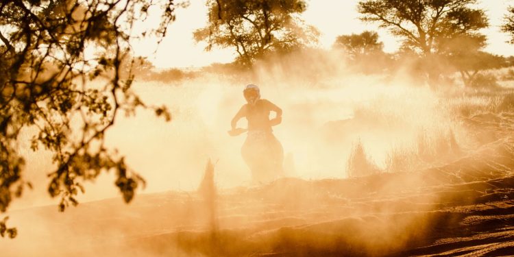 Dynamic shot of a dirt biker riding through a dusty trail with sun setting in the background.