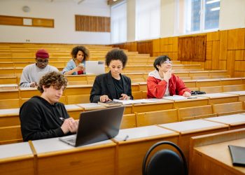 Group of college students studying together in a classroom, focused on learning with laptops and books.