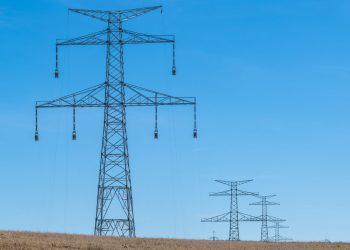 Blue sky over transmission towers on a rural landscape, symbolizing energy distribution.