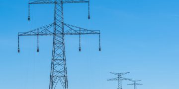 Blue sky over transmission towers on a rural landscape, symbolizing energy distribution.