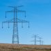 Blue sky over transmission towers on a rural landscape, symbolizing energy distribution.
