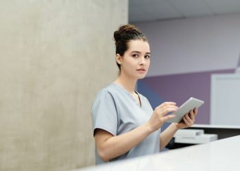 Professional receptionist using a tablet device at a modern office reception desk.