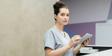 Professional receptionist using a tablet device at a modern office reception desk.