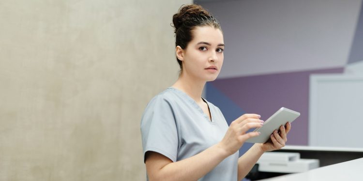 Professional receptionist using a tablet device at a modern office reception desk.