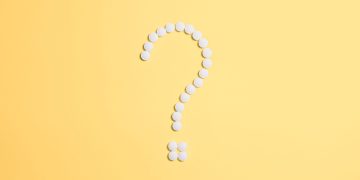 White pills arranged into a question mark shape on a vibrant yellow background.