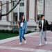Group of young students walking on campus sidewalk on a bright day, showcasing casual university life.