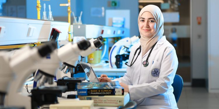 A female scientist in a laboratory setting, conducting research with microscopes and reference books.