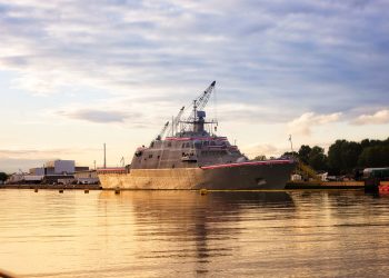 A warship docked in a serene harbor in Marinette, WI, during a golden sunset.