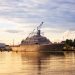 A warship docked in a serene harbor in Marinette, WI, during a golden sunset.