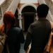 Two university students with backpacks walk down a grand staircase in a historic building.