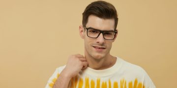 Confident man posing with fashionable eyewear against a warm background.