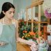 Concentrated female florist with dark hair standing in floral shop with tablet near flowers in wrapper while checking order during work