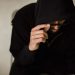 Crop focused male hacker covering head with hood while browsing laptop and lowering eyeglasses in surprise