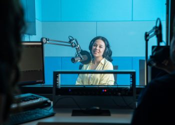 A podcast host records a show in a professional radio studio with microphones and headphones.