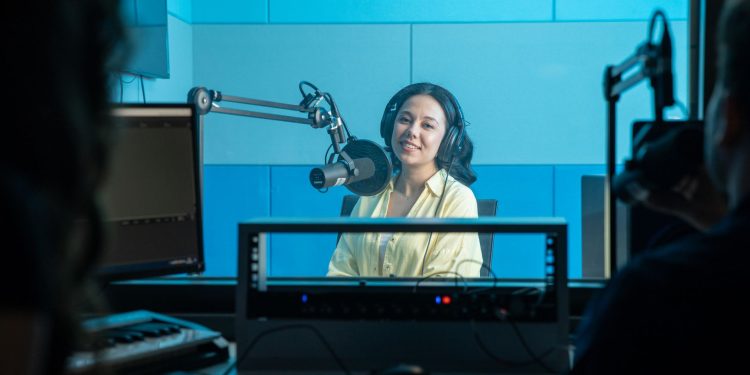 A podcast host records a show in a professional radio studio with microphones and headphones.