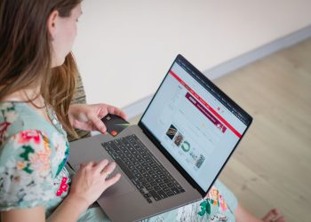 Woman in floral dress shopping online with a laptop and credit card indoors.