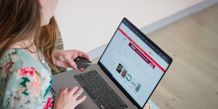 Woman in floral dress shopping online with a laptop and credit card indoors.