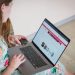 Woman in floral dress shopping online with a laptop and credit card indoors.