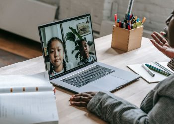 From above of crop confident African American female teacher sitting in classroom and teaching multiethnic pupils remotely on laptop during coronavirus pandemic